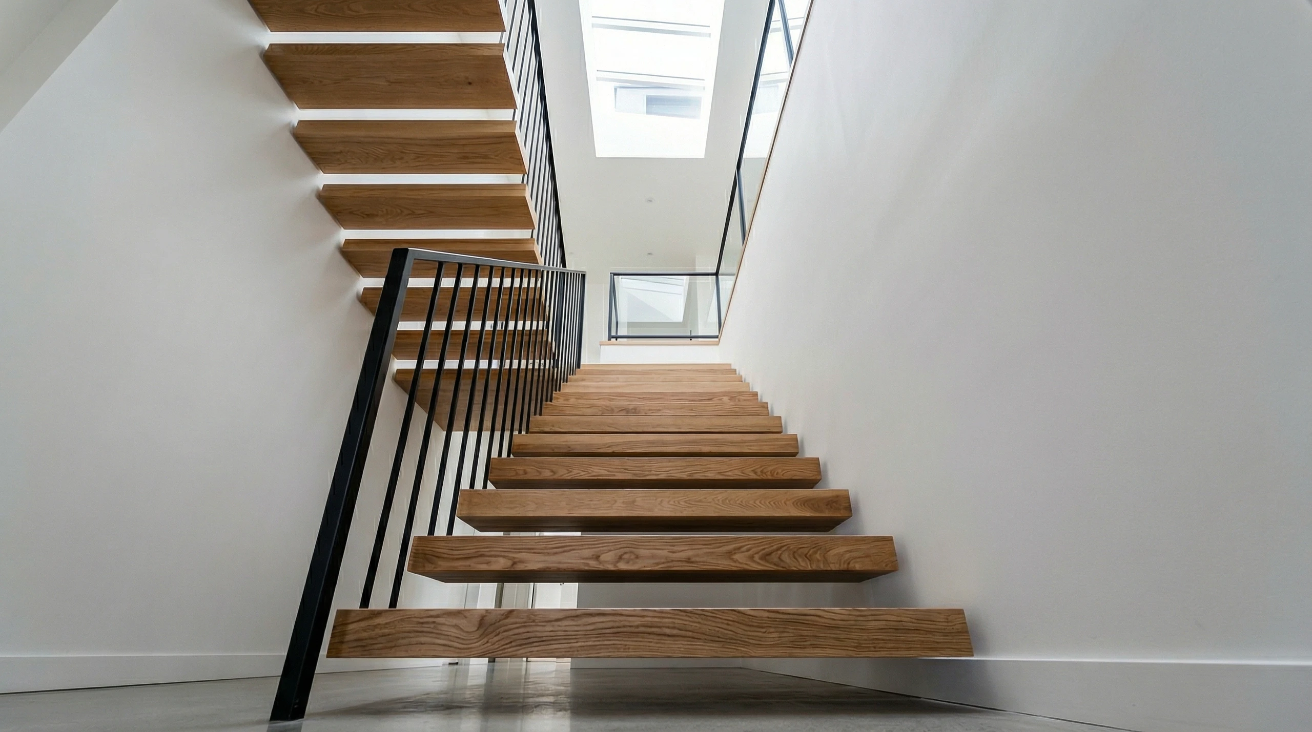 Nowoczesne schody dywanowe z litego drewna i czarną metalową balustradą we wnętrzu