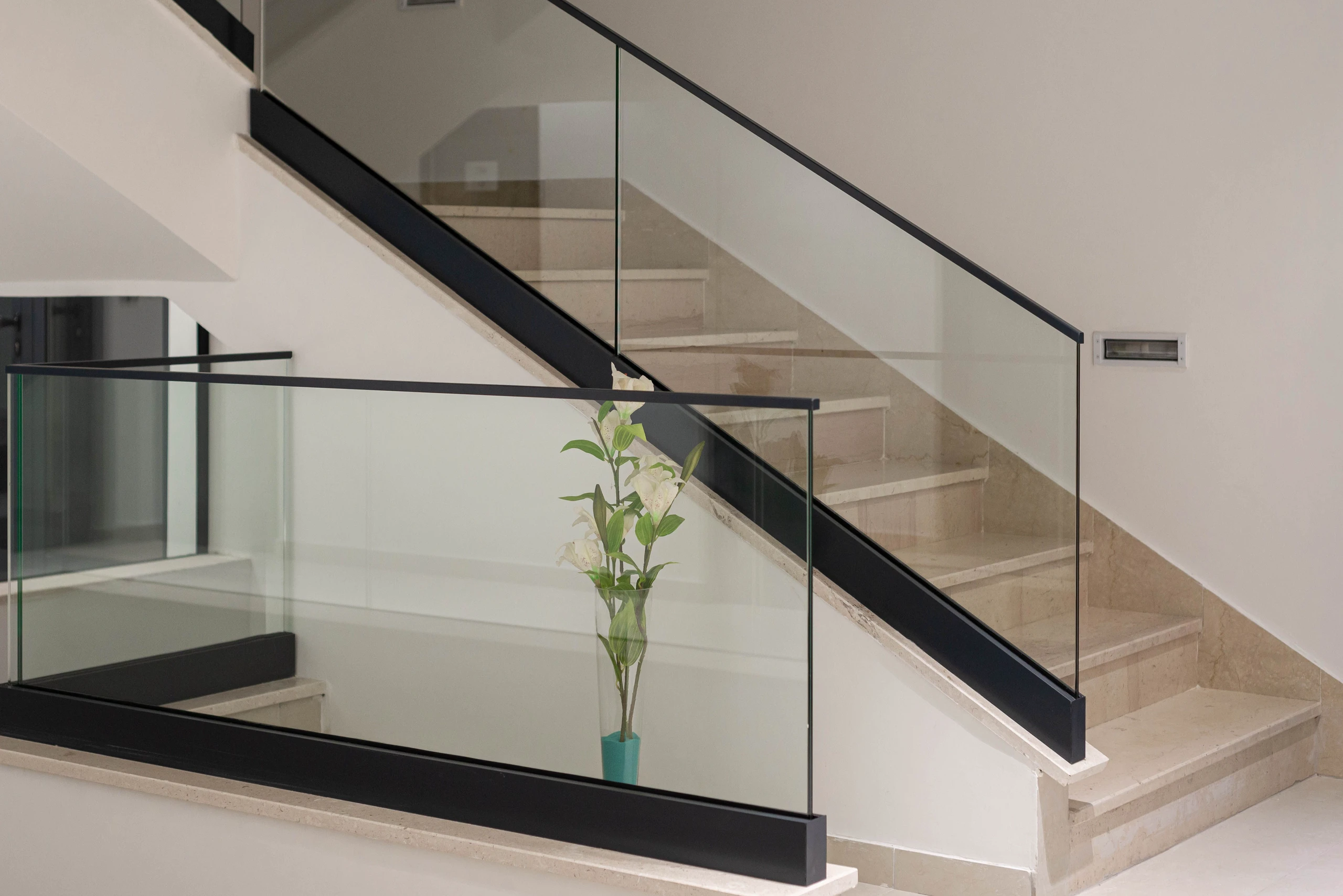 Balustrady szklane z czarną metalową poręczą na kamiennych schodach we wnętrzu