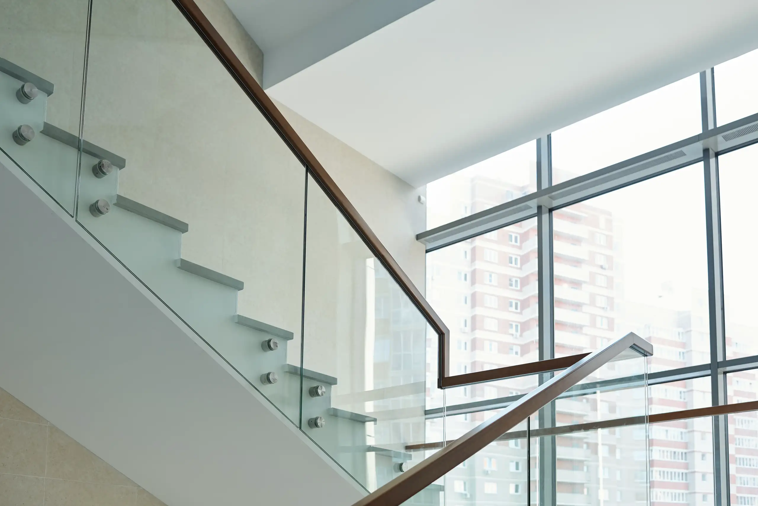 Szklane balustrady schodów wewnętrznych z drewnianą poręczą i betonowymi stopniami przy dużych oknach