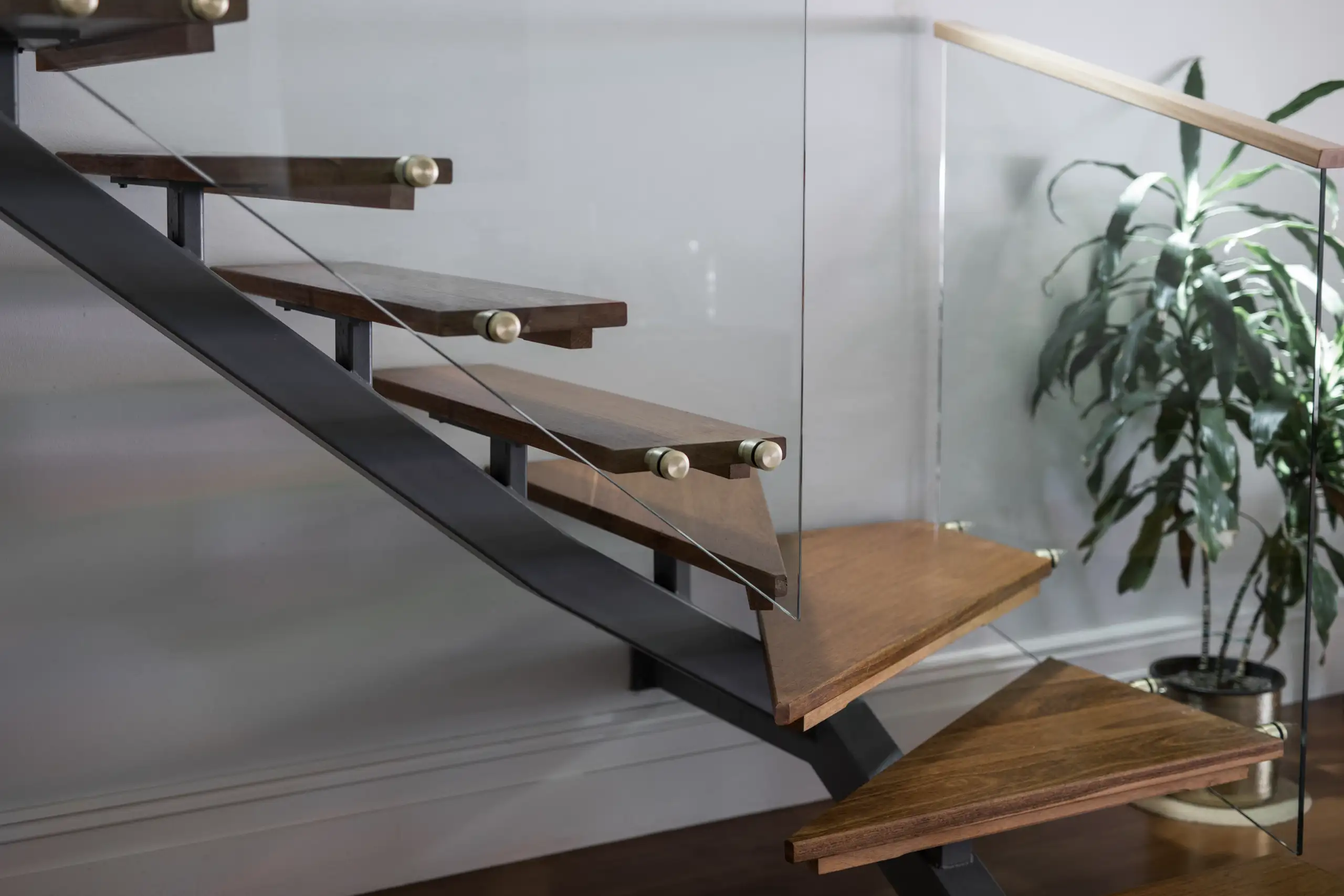 Nowoczesne schody samonośne z drewnianymi stopniami i szklaną balustradą w minimalistycznym wnętrzu