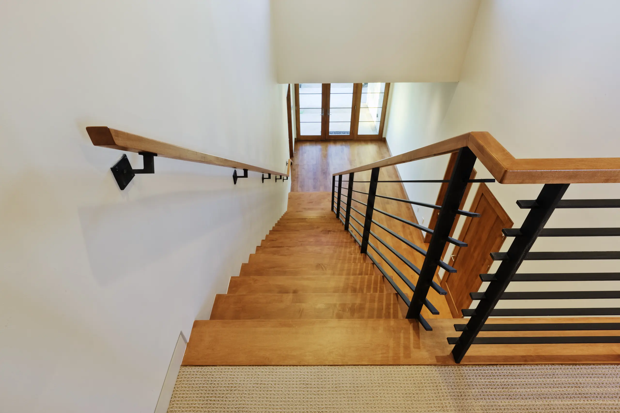 Schody nowoczesne z drewnianymi stopniami, czarną metalową balustradą i drewnianą poręczą